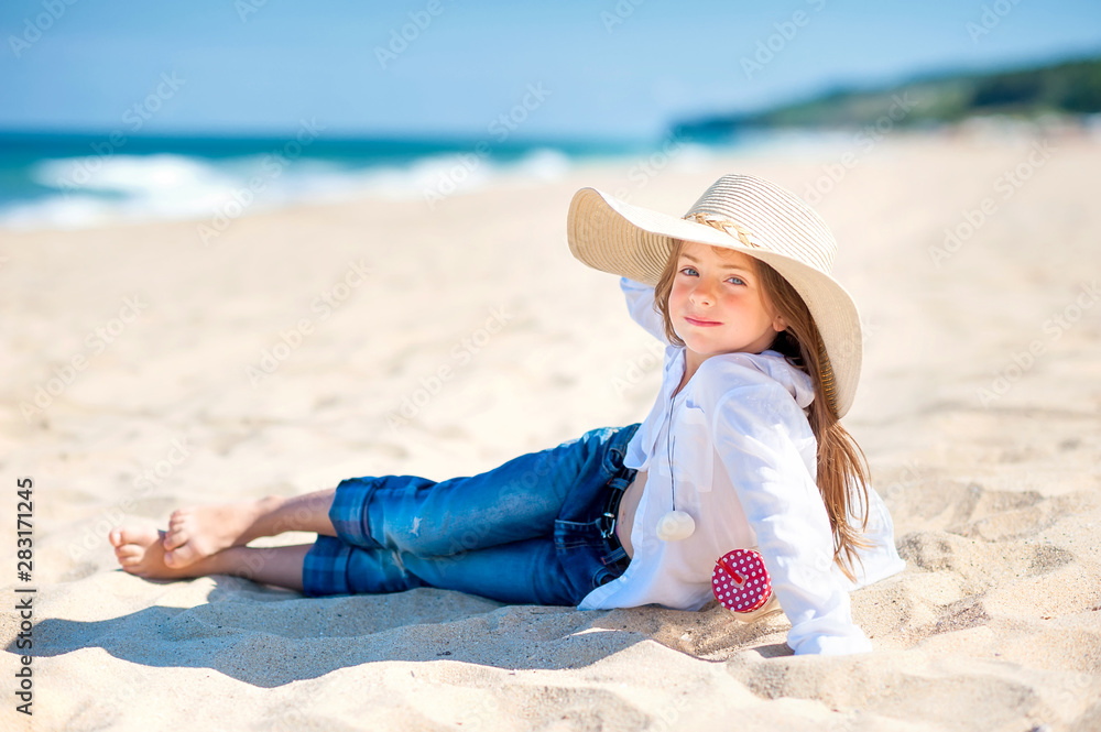 Cute little girl in a hat is resting on the beach, summer trip, vacation