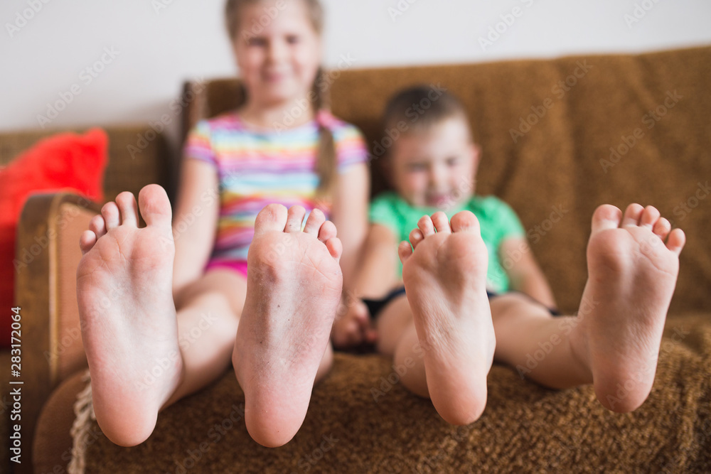 Naklejka premium Close-up focus on the toes of two children sitting next to the sofa - faces out of focus