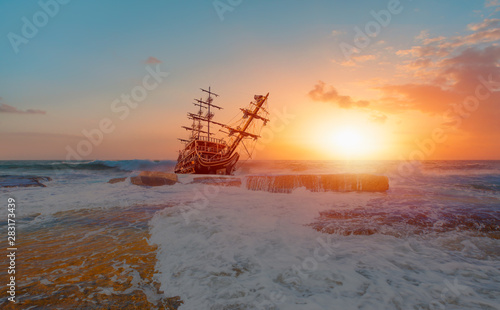 Sailing old ship in storm sea against dramatic sunset