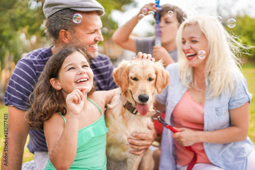 Happy family doing picnic in nature outdoor - Young parents having fun with children and their dog in summer time laughing, playing together with soap bubbles - Focus on female kid hand