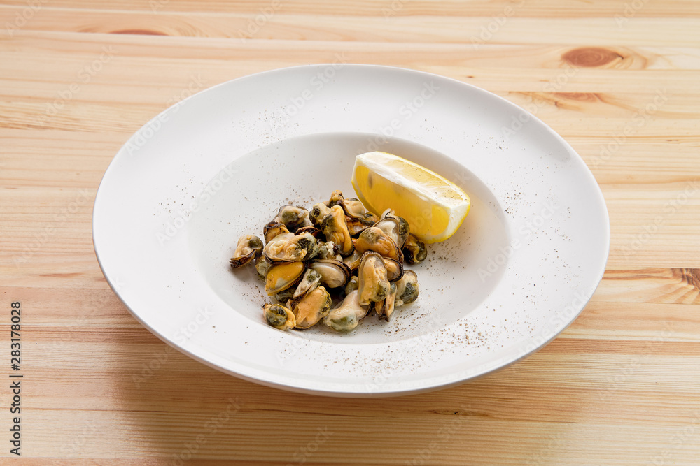 Plate with marinated mussels and slice of lemon on wooden table