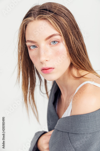 Portrait of slim brown-haired young woman in male jacket looking at camera isolated on white background