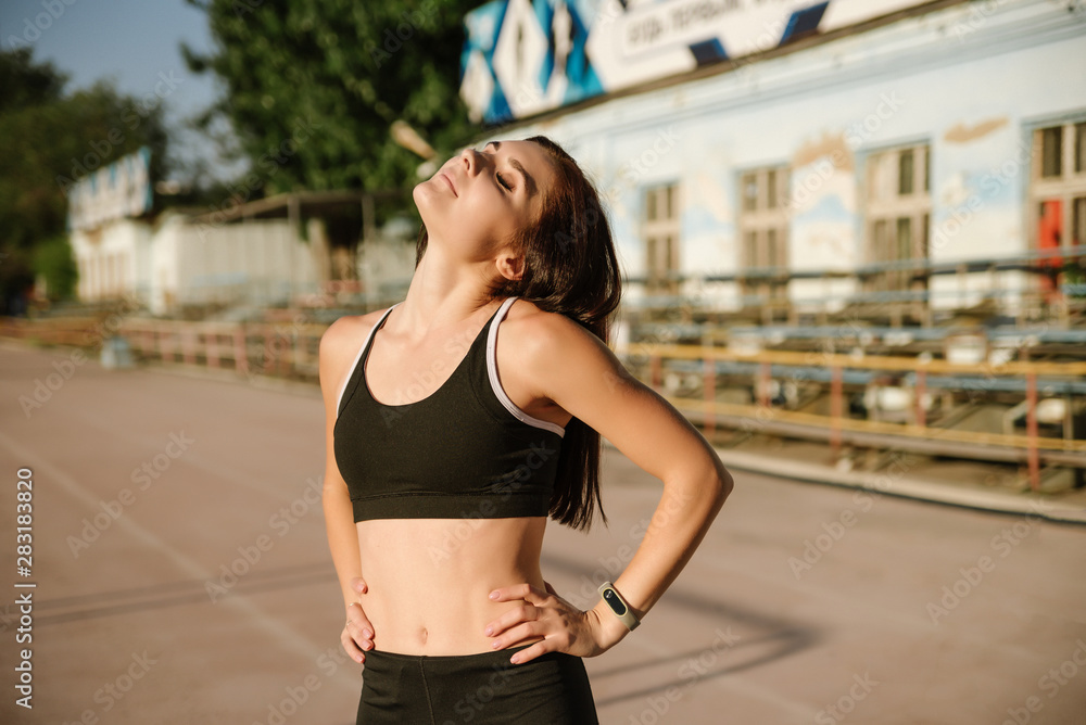 A beautiful sports girl in black sportswear is doing a warm-up at the stadium. The concept of a healthy lifestyle.