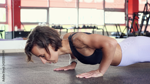 Bilde på lerret Sporty woman is doing set of reps press-ups from the floor in gym