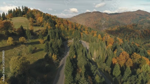 picturesque grey winding road among thick forests and green meadows on hills lit by autumn sunlight upper view. Carpathian mountains, Ukraine beauty nature. Travel, summer holiday, wild recreation. 4K photo