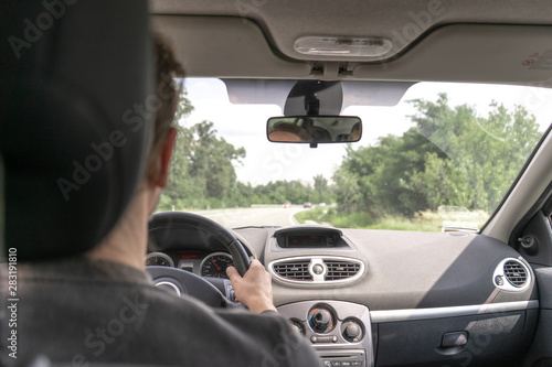 Close-up. Man driving the car on the road in the city on a summer day. Man's hand on the gearbox. Dashboard and instrument panel. View from the back  © MoonfliesPhoto