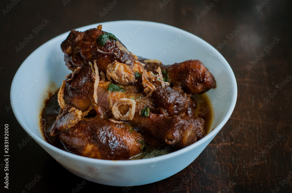 Malaysian dish of Ayam Masak Kicap or deep fried chicken in black soy gravy in a white bowl. Malaysian dish of Ayam Masak Kicap or deep fried chicken in black soy gravy in a white bowl.