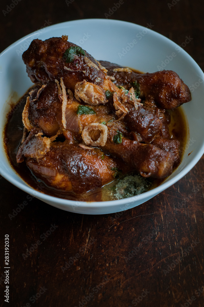 Malaysian dish of Ayam Masak Kicap or deep fried chicken in black soy gravy in a white bowl. Malaysian dish of Ayam Masak Kicap or deep fried chicken in black soy gravy in a white bowl.