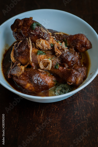 Malaysian dish of Ayam Masak Kicap or deep fried chicken in black soy gravy in a white bowl.