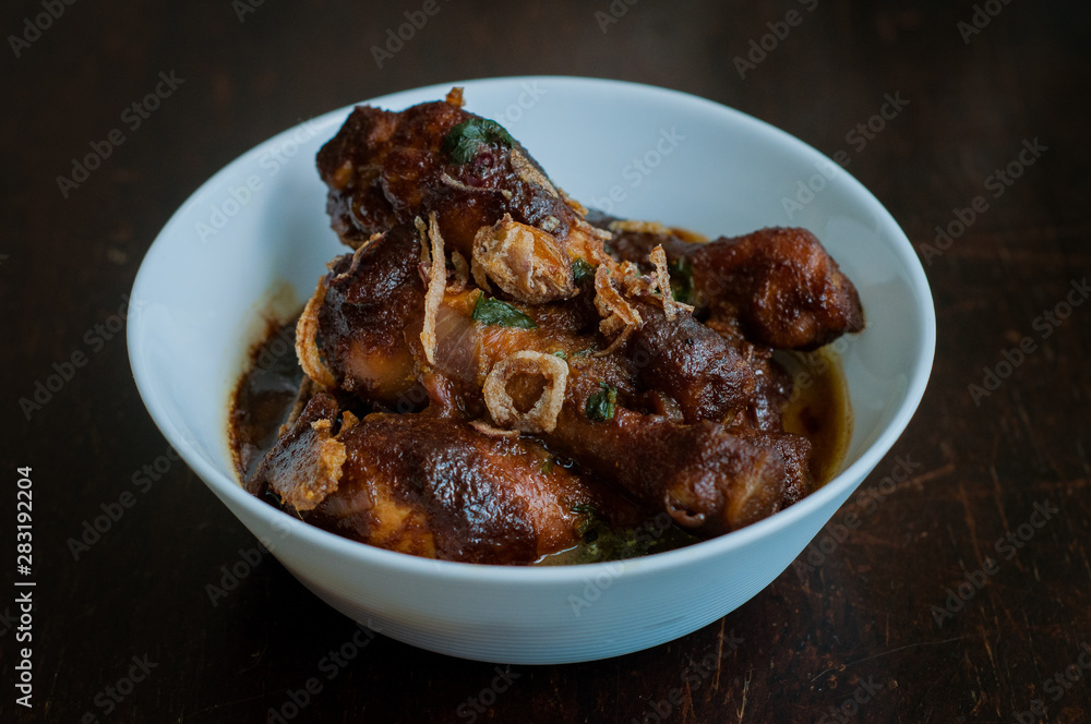 Malaysian dish of Ayam Masak Kicap or deep fried chicken in black soy gravy in a white bowl. Malaysian dish of Ayam Masak Kicap or deep fried chicken in black soy gravy in a white bowl.