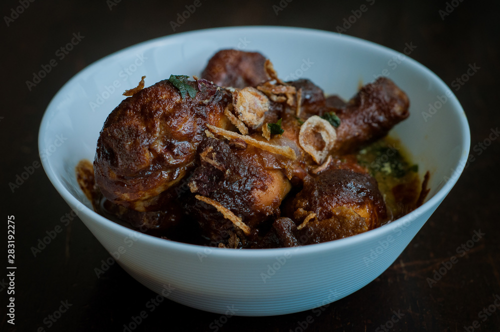 Malaysian dish of Ayam Masak Kicap or deep fried chicken in black soy gravy in a white bowl. Malaysian dish of Ayam Masak Kicap or deep fried chicken in black soy gravy in a white bowl.