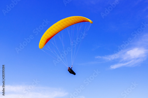 Paraglider flying on the background of blue sky with clouds, freedom concept.