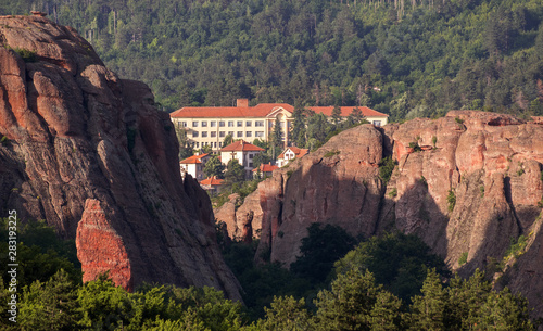 Magnificent rocks on the background of buildings among the forest at sunset. Belogradchik, Bulgaria.