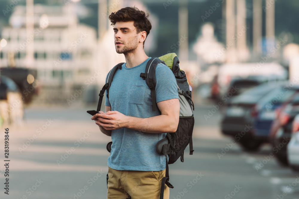 handsome man in t-shirt holding smartphone and looking away