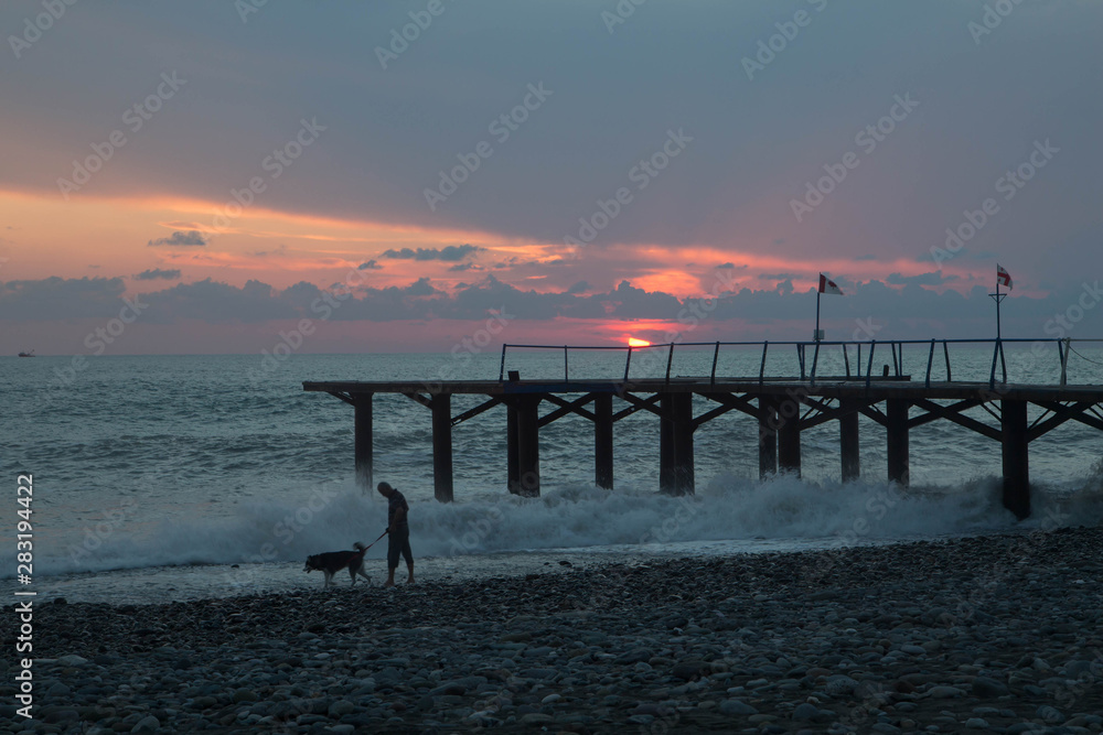sun setting over Batumi beach Dock, as powerful waves roll in, and a very colorful sky is reflected on the beach