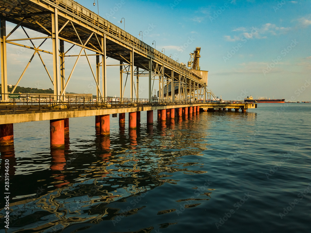 A dry cargo pier on a clear sunny day on stilts stands in the water of the sea with small waves.