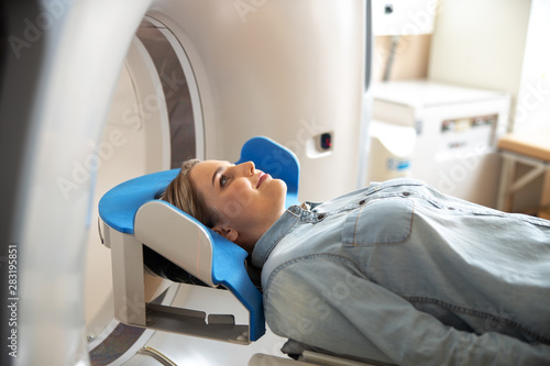Joyful young woman lying on CT scanner table at radiology clinic