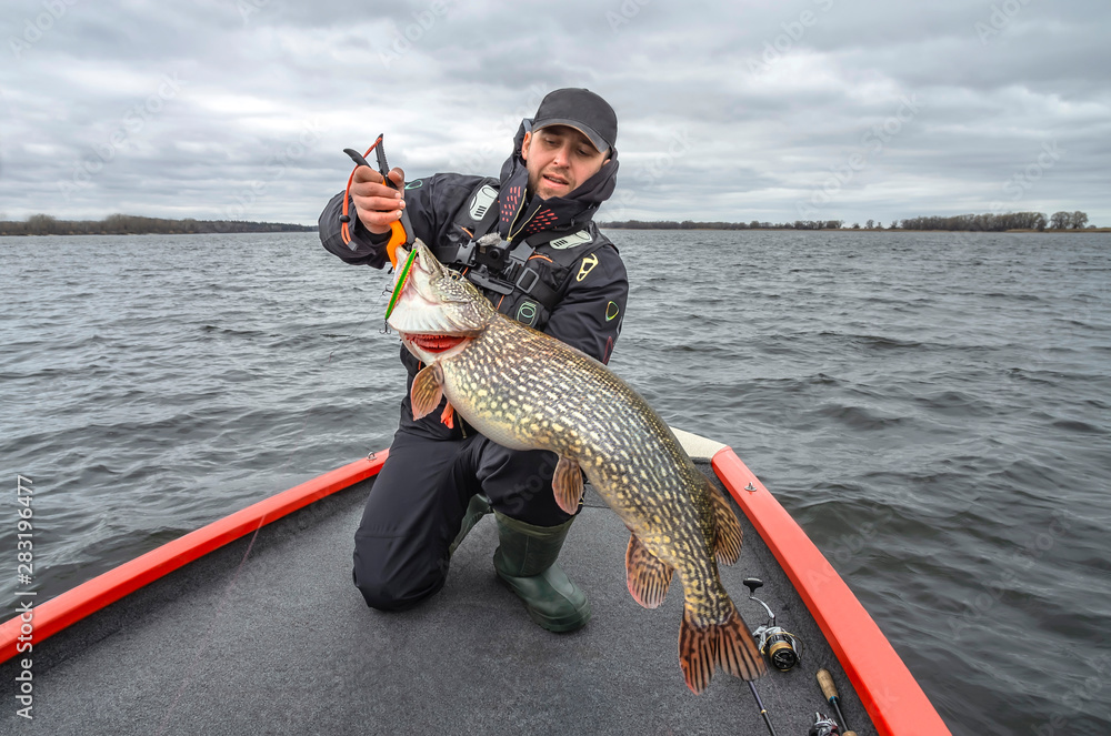 Pike fishing. Happy fisherman with big fish trophy at the boat with tackles Pike fishing. Happy fisherman with big fish trophy at the boat with tackles