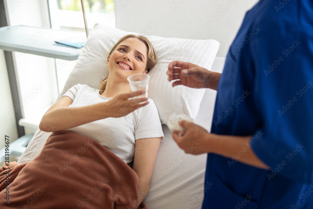 Obraz premium Smiling lady holding cup of water and looking at doctor