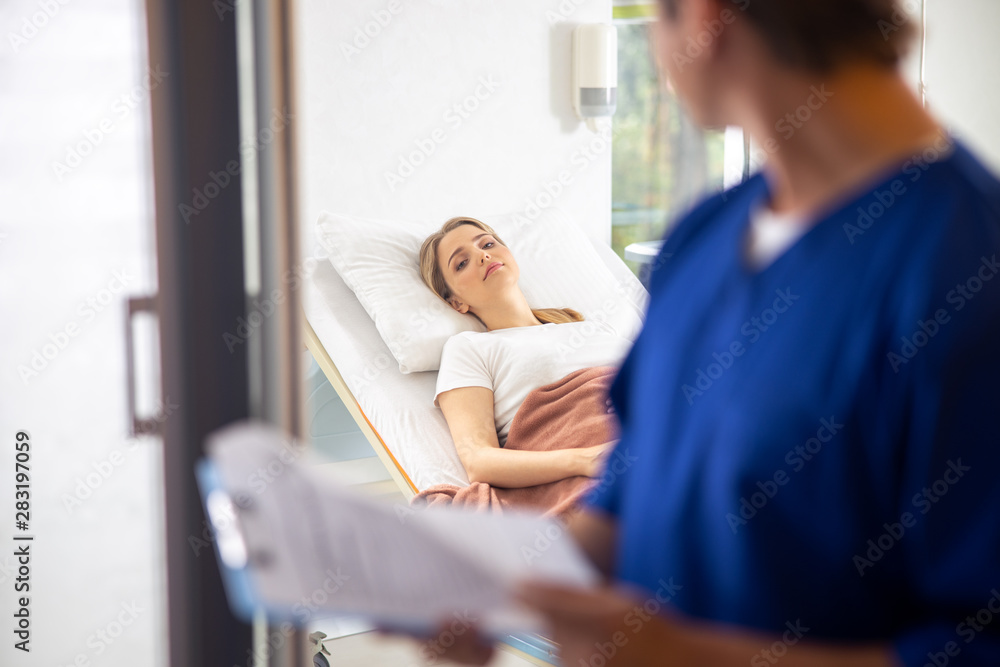 Young lady lying in bed and looking at doctor Young lady lying in bed and looking at doctor