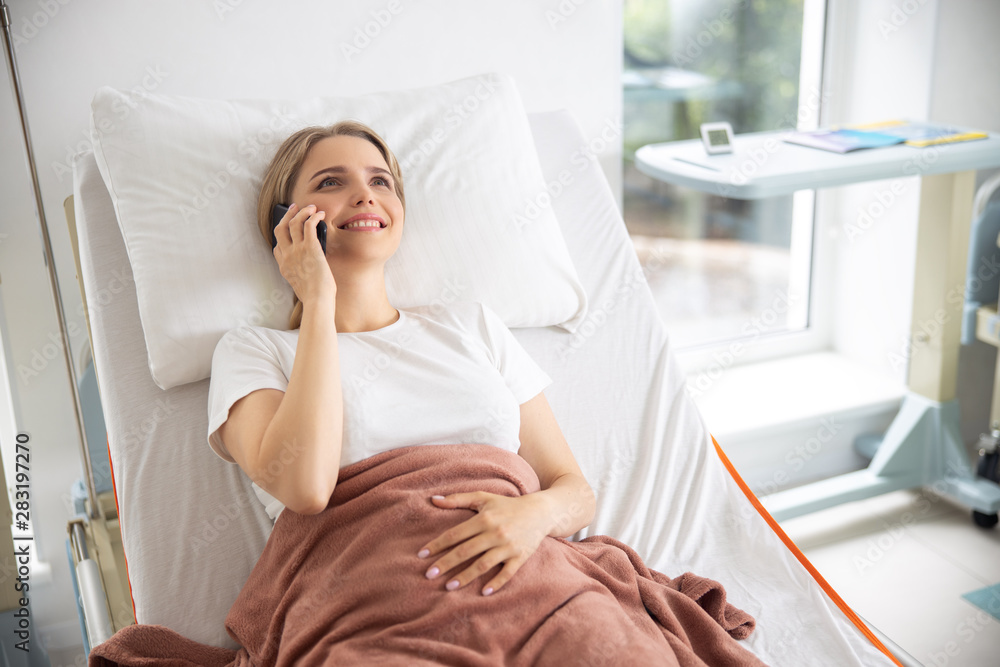 Smiling lady having phone conversation in hospital room Smiling lady having phone conversation in hospital room