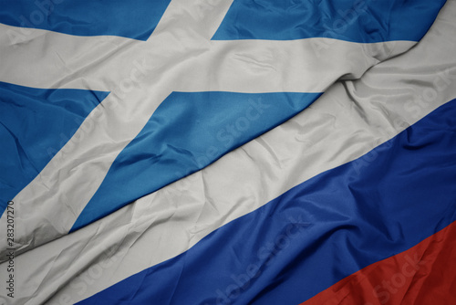 waving colorful flag of russia and national flag of scotland.