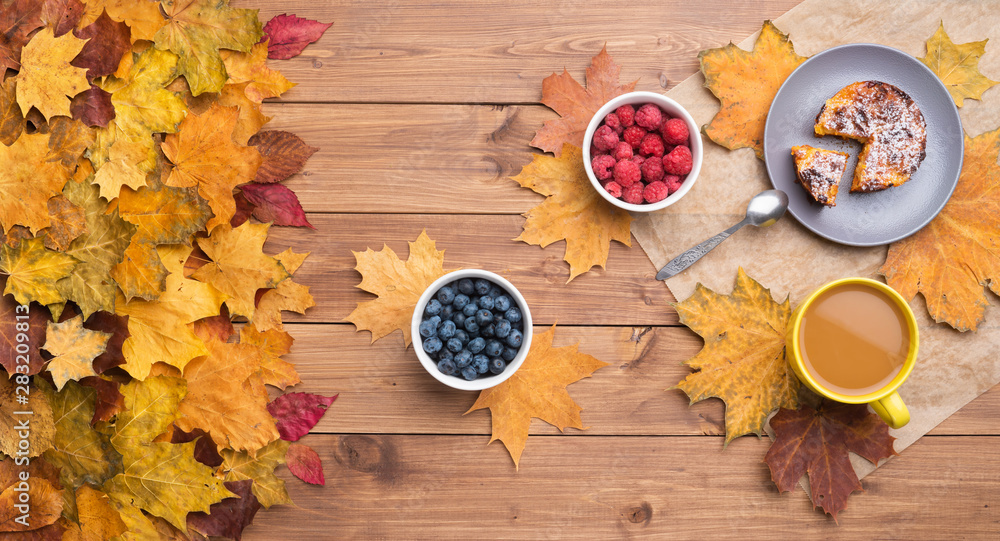 Seasonal autumn background. Frame of maple leaves and a cake and berries over wooden background.