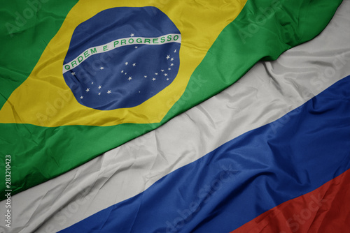 waving colorful flag of russia and national flag of brazil.