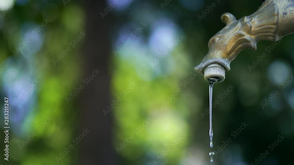 Light stream of crystal clear water pouring slowly from the iron tap. Small blue water drops falling from bronzed tap, abstract water motion. Hydration system in ecology Light stream of crystal clear water pouring slowly from the iron tap. Small blue water drops falling from bronzed tap, abstract water motion. Hydration system in ecology