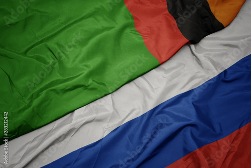 waving colorful flag of russia and national flag of zambia.