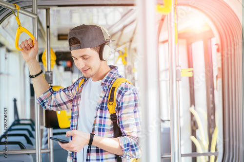 Everyday life and commuting to work or study by bus tram concept. Handsome student man with headphones is paying transport ticket with mobile phone.