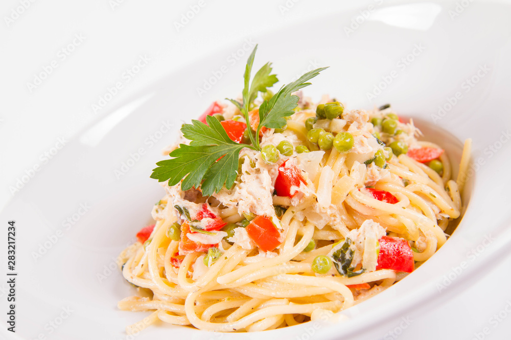 Spaghetti with cream sauce with smoked mackerel, peas ,bell pepper and some parsley on a white plate on a white background