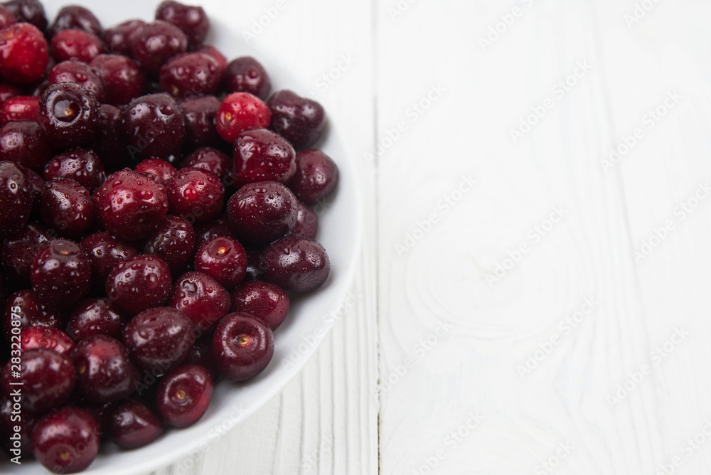 A lot of fresh sweet cherry fruit berries with water drops, close up on the plate on white background. Close up of pile of ripe cherries. Large collection of fresh red cherries. Ripe cherries texture A lot of fresh sweet cherry fruit berries with water drops, close up on the plate on white background. Close up of pile of ripe cherries. Large collection of fresh red cherries. Ripe cherries texture