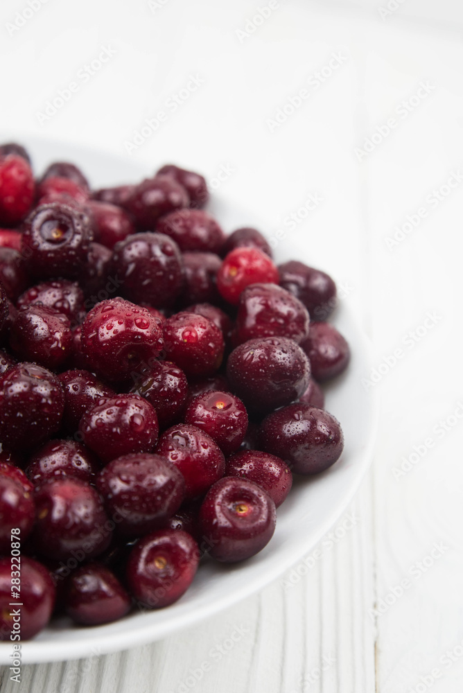 A lot of fresh sweet cherry fruit berries with water drops, close up on the plate on white background. Close up of pile of ripe cherries. Large collection of fresh red cherries. Ripe cherries texture A lot of fresh sweet cherry fruit berries with water drops, close up on the plate on white background. Close up of pile of ripe cherries. Large collection of fresh red cherries. Ripe cherries texture