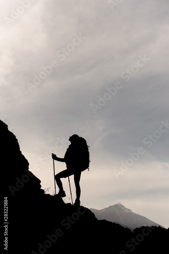 Dark silhouette girl standing on the rocks with hiking backpack and walking sticks
