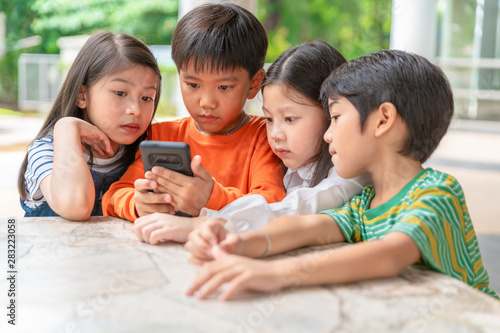 group of asian kids play game on smartphone together  smiling small brother and sister have fun hold using cellphone  watch funny cartoon. Children and technology concept