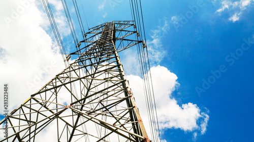 Electricity pylons with blue sky and white clouds. High voltage grid tower with wire cable at distribution station. High voltage electric tower and transmission lines.