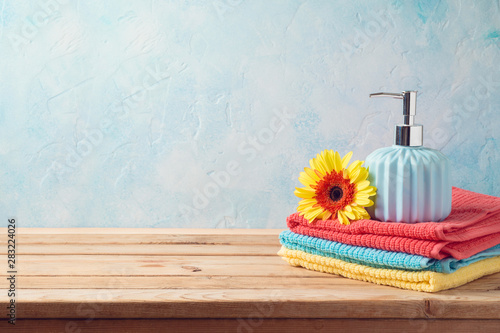 Bath towels and soap bottle on wooden table over bathroom wall background