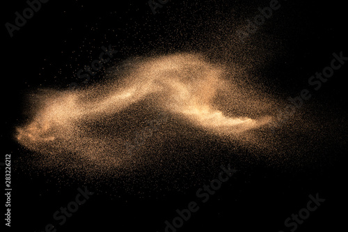 Brown colored sand splash against dark background. Dry river sand explosion isolated on black background. Abstract sand cloud.