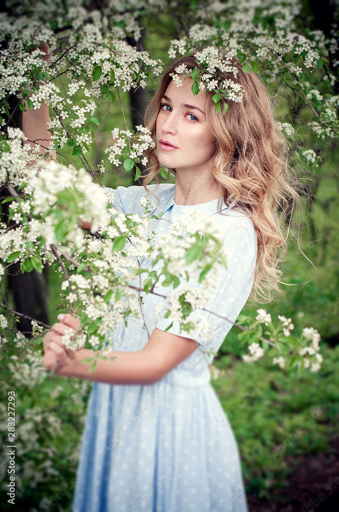 Beautiful happy young woman enjoying smell in a flowering spring garden. Blonde with blue eyes and blue dress. Beautiful happy young woman enjoying smell in a flowering spring garden. Blonde with blue eyes and blue dress.