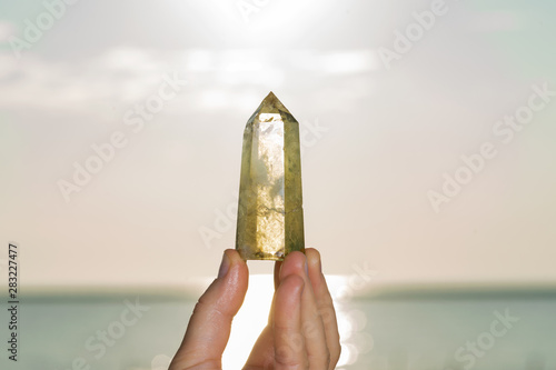 Tableau sur toile Woman holding Polished CITRINE point in her hand at sunrise in front of the lake