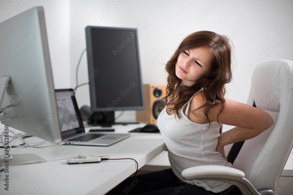Woman working on a computer in a home office - suffering form lower back pain Woman working on a computer in a home office - suffering form lower back pain