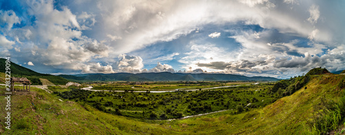 Panorama of lush green river valley at sunset with sun rays and dramatic sky. The area is known as Shangri-la. North Yunnan, China.