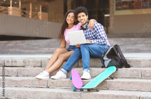 Couple of black teens sitting on stairs with laptop