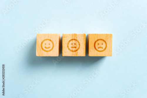 Happy, neutral and frown face on wood blocks toys and blue background. Rating concept.