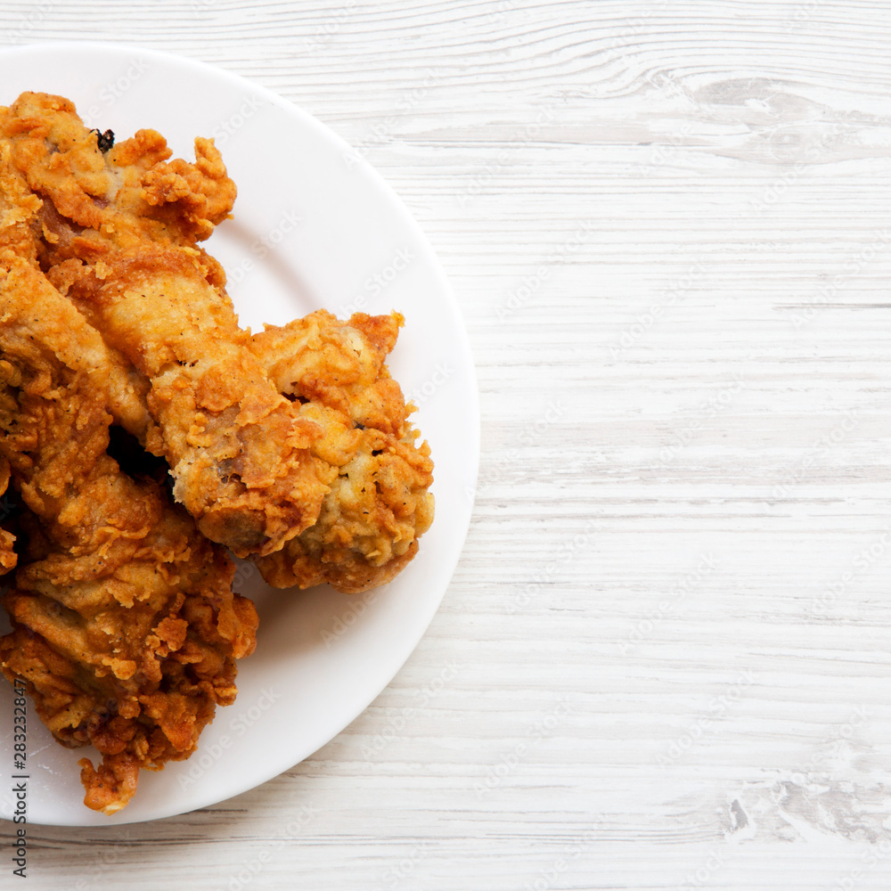 Fried chicken drumsticks on a white round plate on a white wooden background, top view. From above, overhead, flat lay. Copy space. Fried chicken drumsticks on a white round plate on a white wooden background, top view. From above, overhead, flat lay. Copy space.