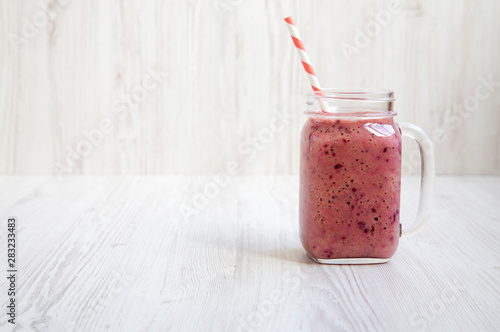 Mason glass jar mug filled with banana, black currant, coconut milk smoothie on a white wooden background, side view. Space for text. photo