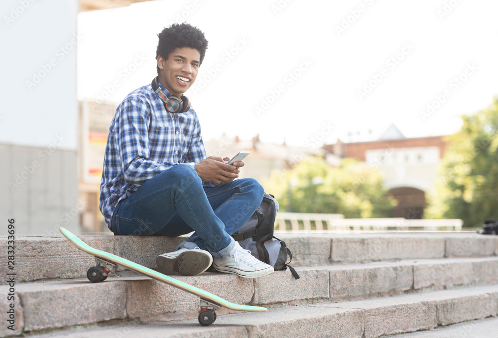 Obraz premium Cheerful teenager using smartphone sitting on stairs against cityscape