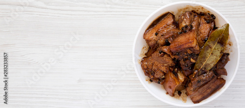 Homemade Filipino Adobo Pork in a white bowl over white wooden background, top view. Flat lay, from above, overhead. Space for text. photo