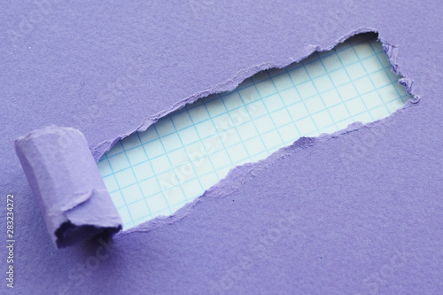 a hole with torn edges of purple paper and checkered paper in the background. Space for text...